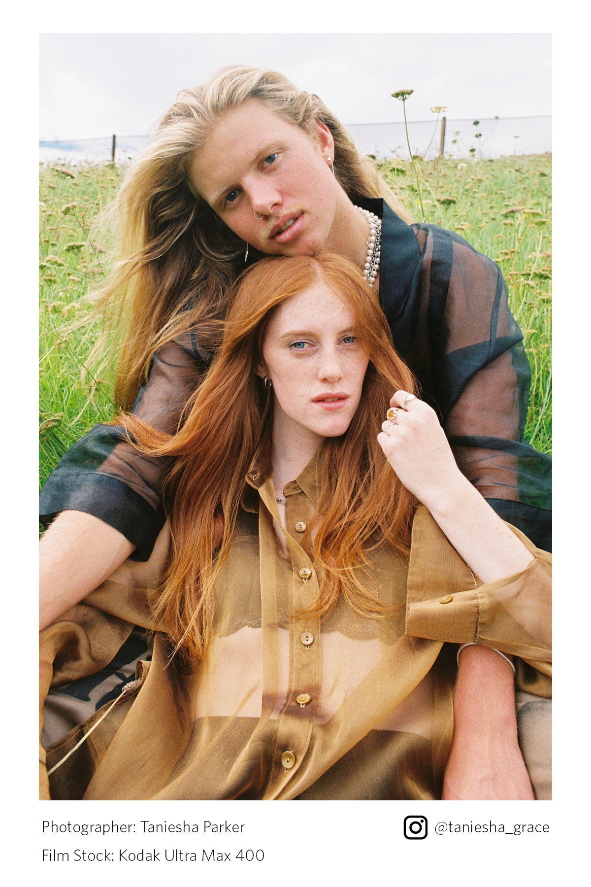 Two people sitting in a grassy field with a clear sky.