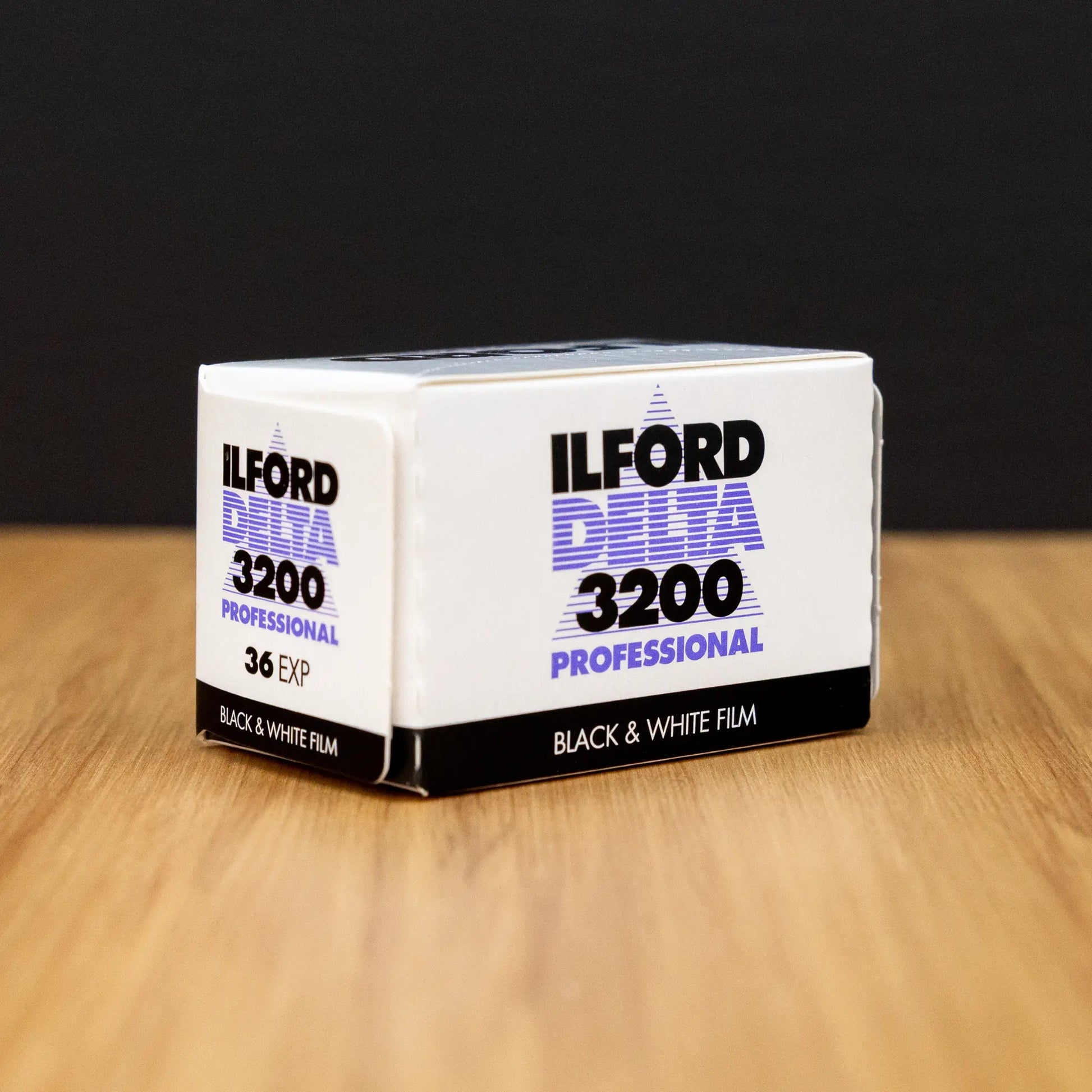 Ilford Delta 3200 black and white film box at 3/4 view on a wooden surface with a dark background