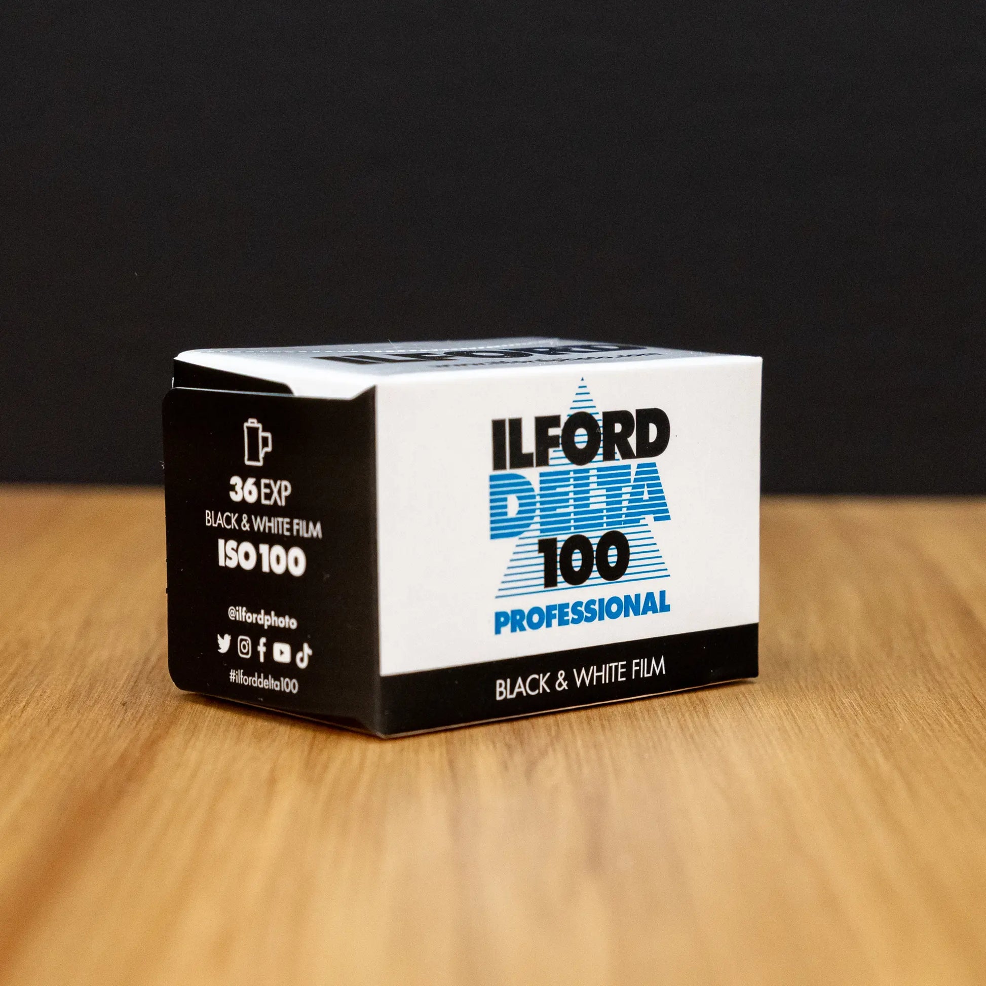 Ilford Delta 100 black and white film box on a wooden surface with a dark background