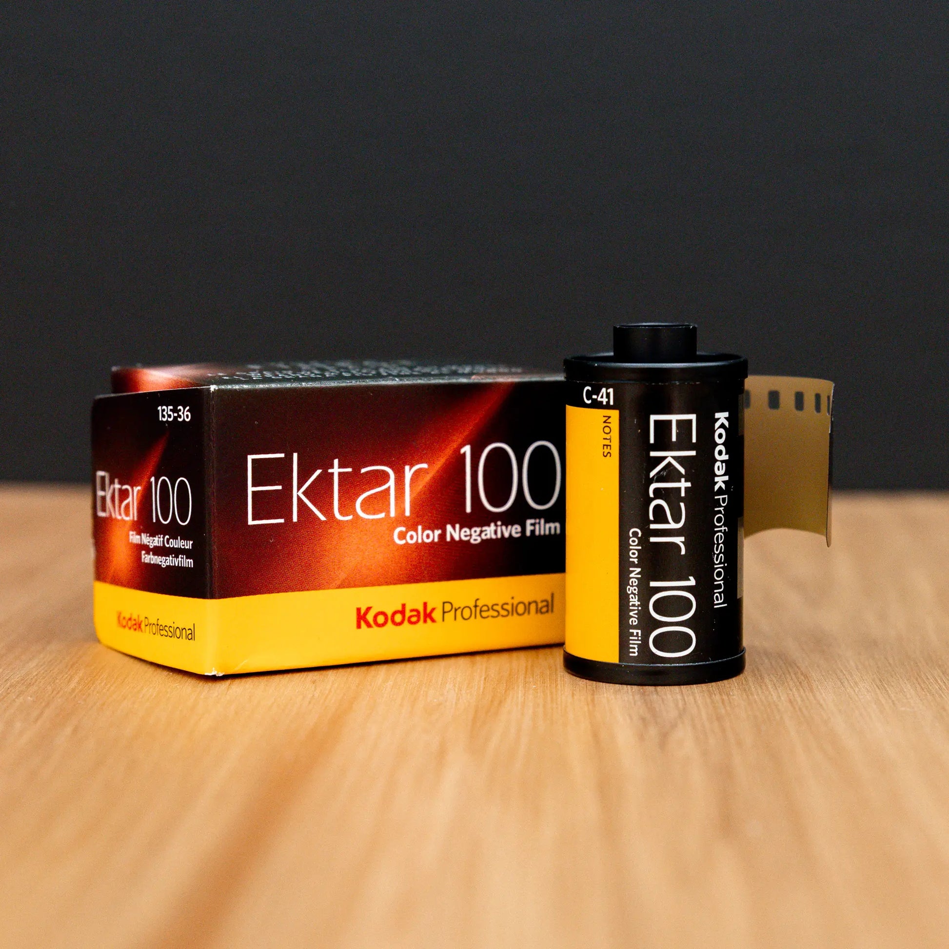 Kodak Ektar 100 film canister and packaging on a wooden surface with a black background