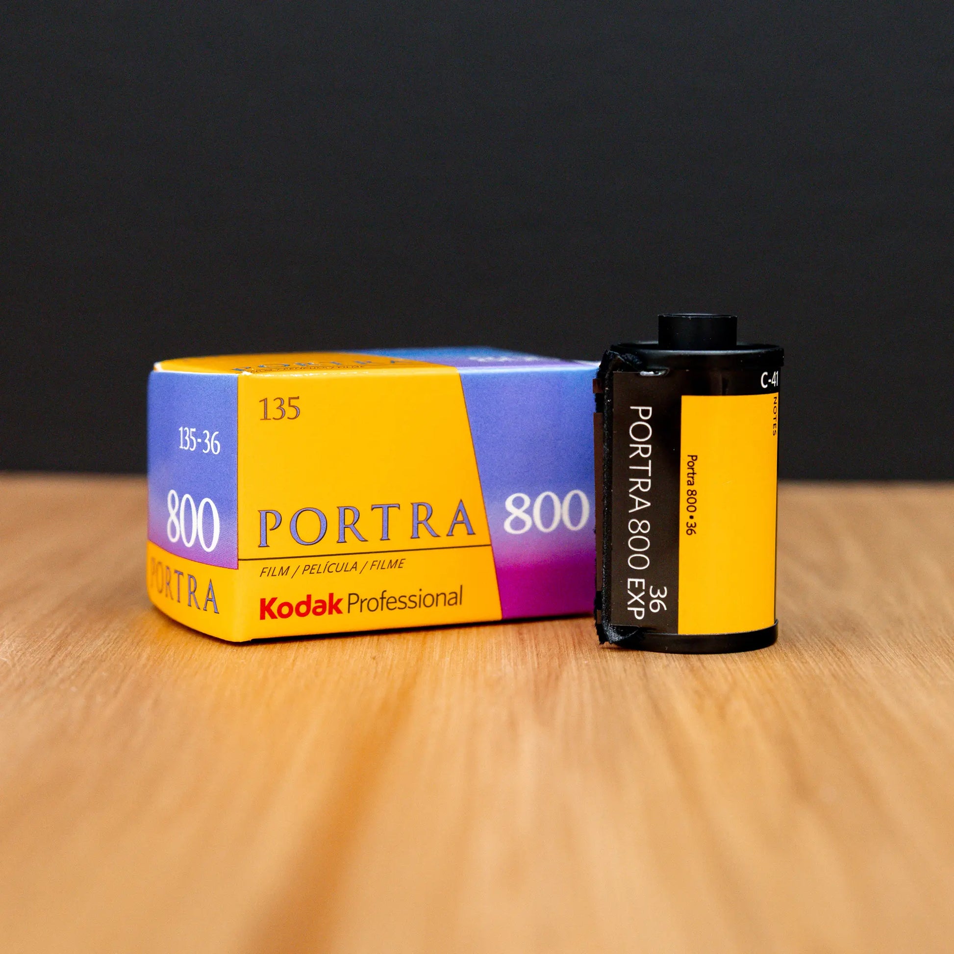 Kodak Portra 800 film canister and packaging 3/4 view on a wooden surface with a black background