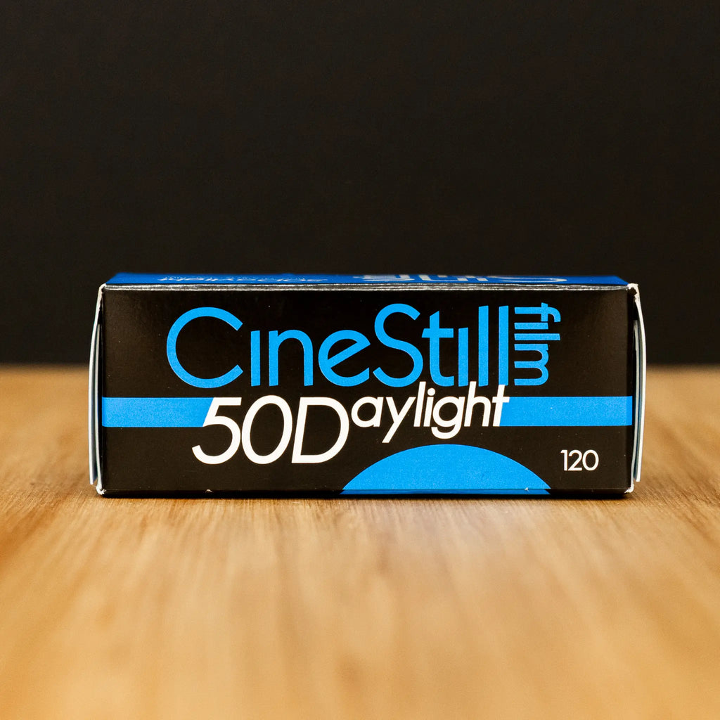 CineStill 50D Daylight film packaging on a wooden surface with a black background