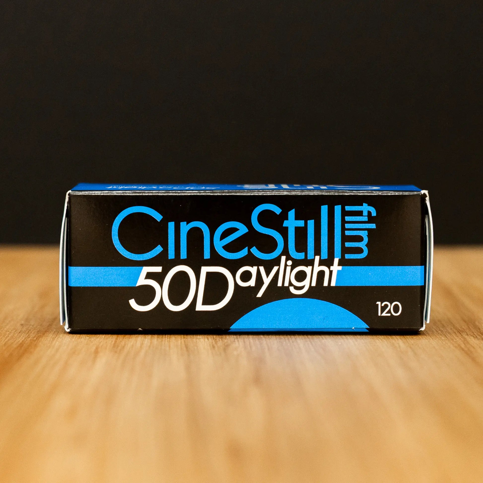 CineStill 50D Daylight film packaging on a wooden surface with a black background