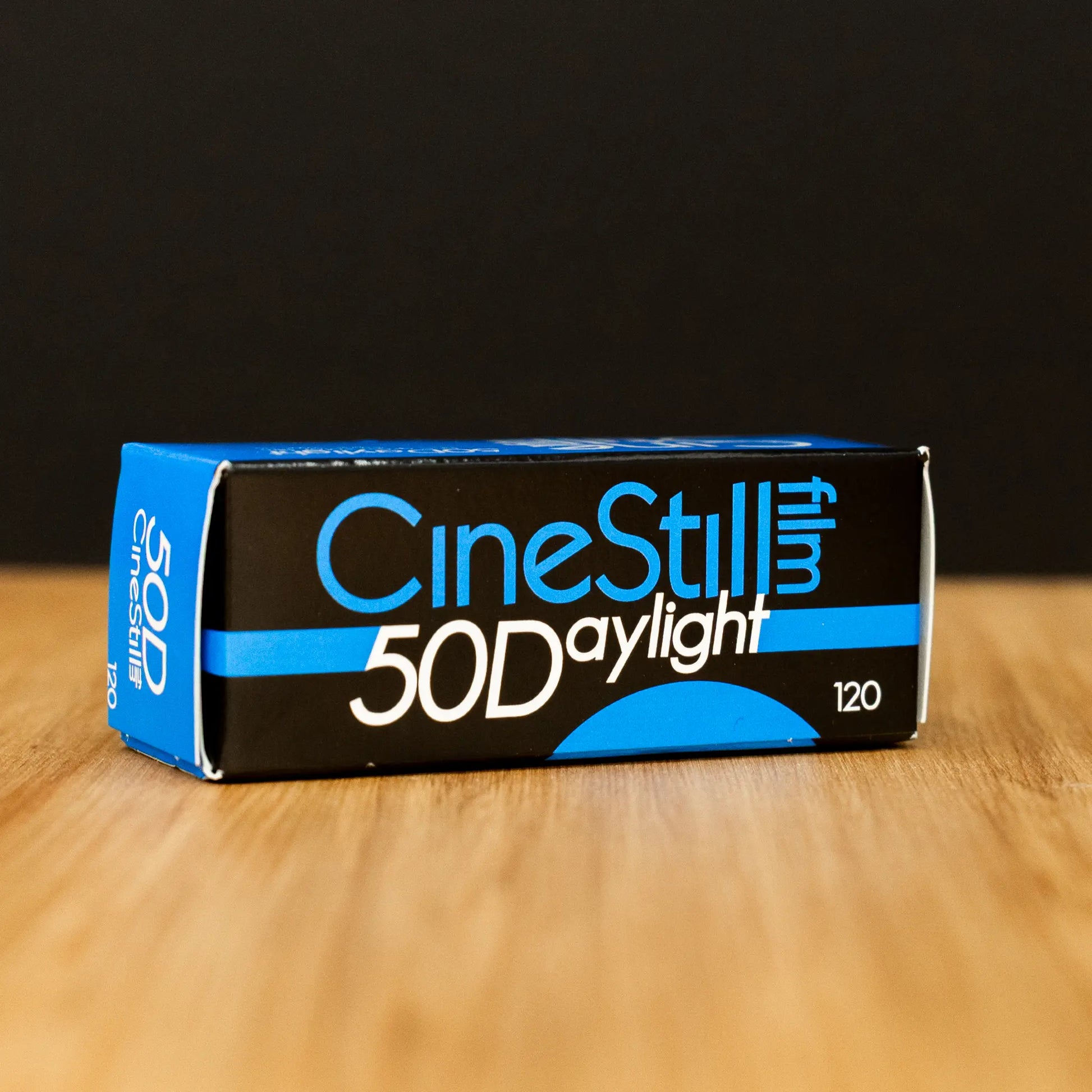 CineStill 50D daylight film box on a wooden surface with a black background