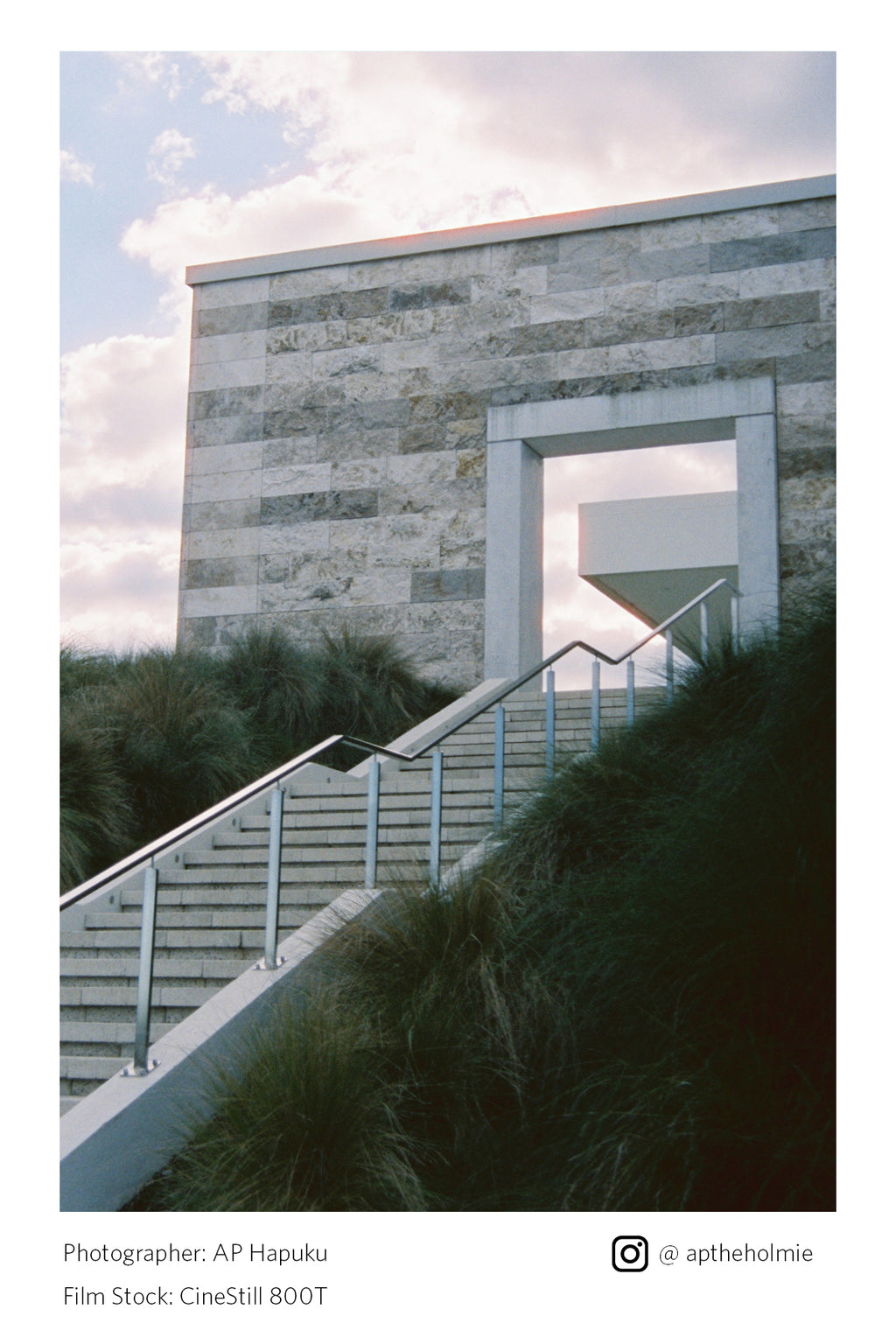 Modern building with stone facade and metal staircase, surrounded by grass and sky shot on Cinestill 800T