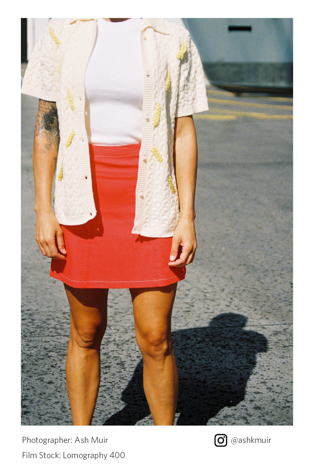Person wearing a red skirt and white top with a beige cardigan on a street Shot on Lomography 400