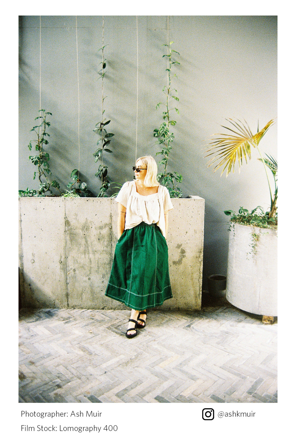 Woman in a white top and green skirt standing in a room with plants and concrete walls shot on Lomography 400