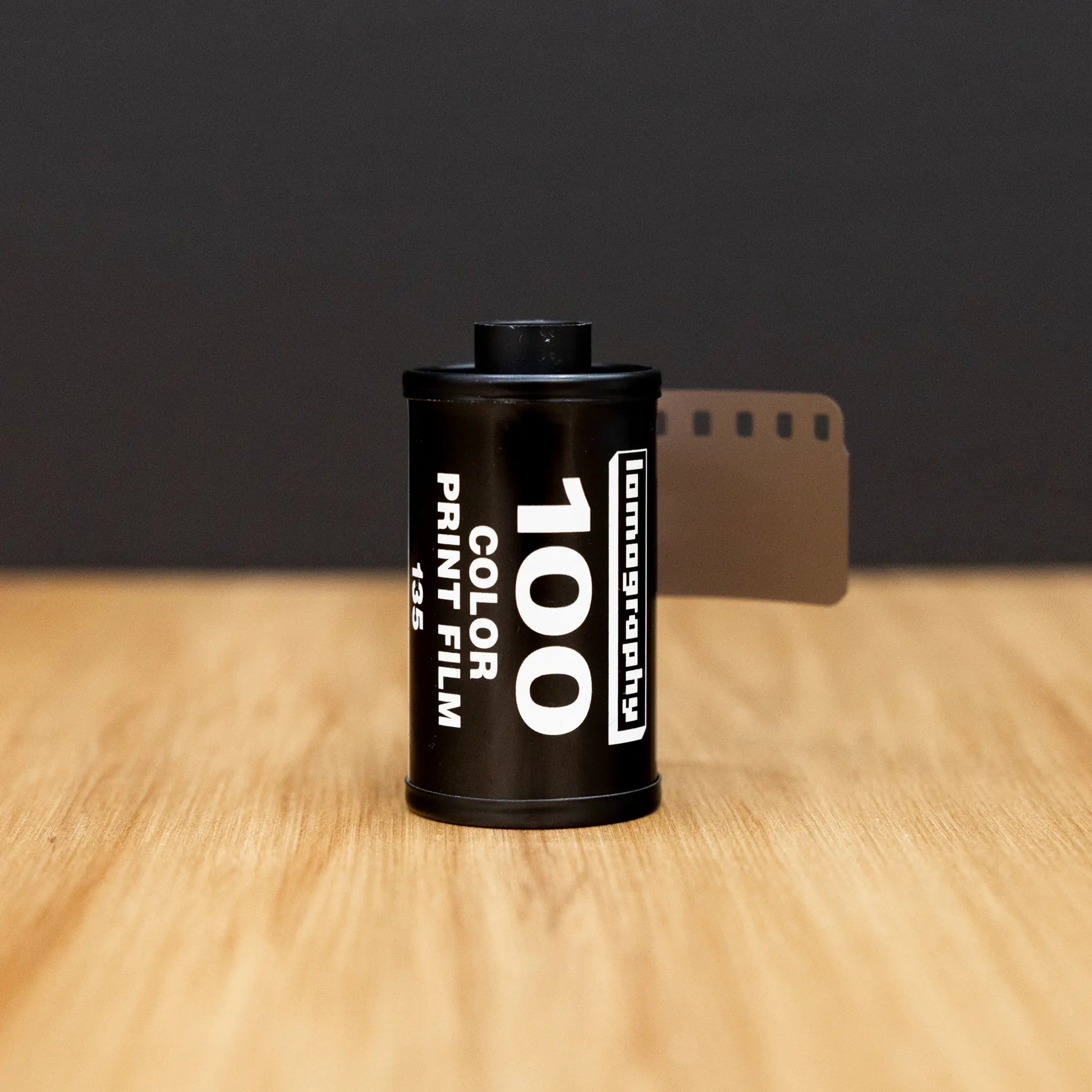 Film canister with '100 Color Print Film' text on a wooden surface and black background