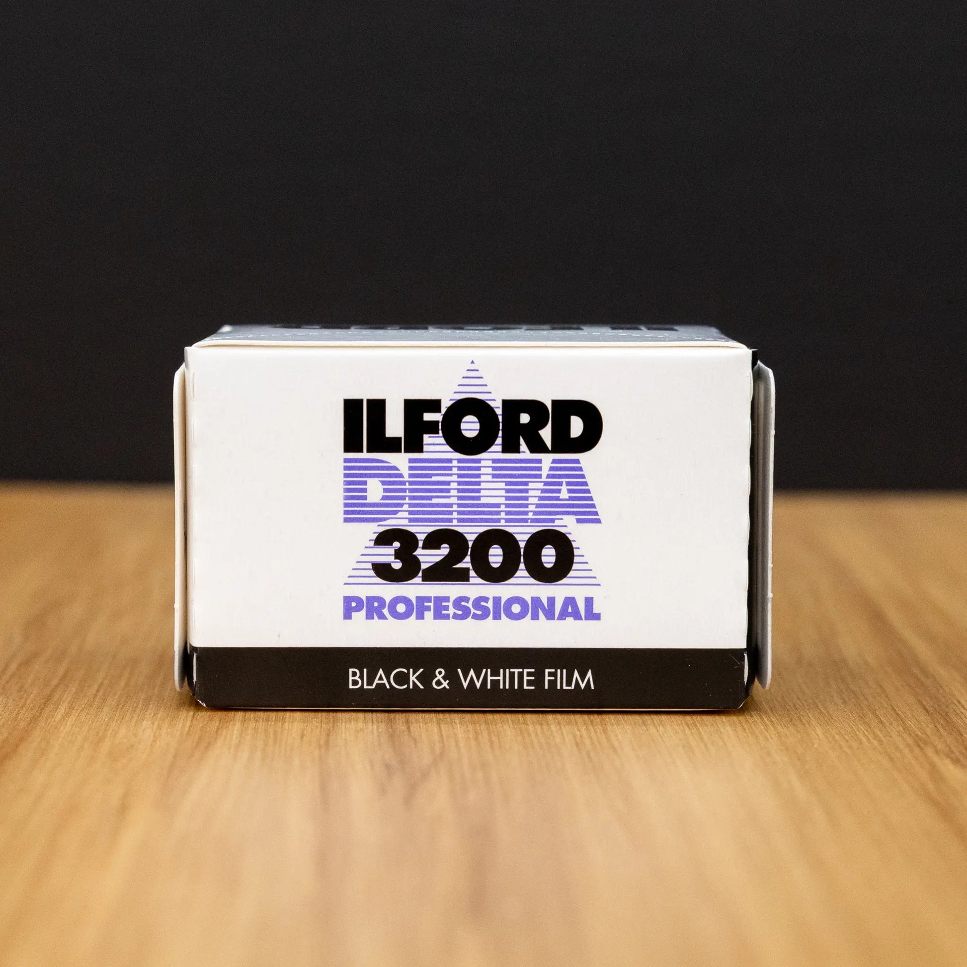 Ilford Delta 3200 black and white film packaging on a wooden surface with a dark background
