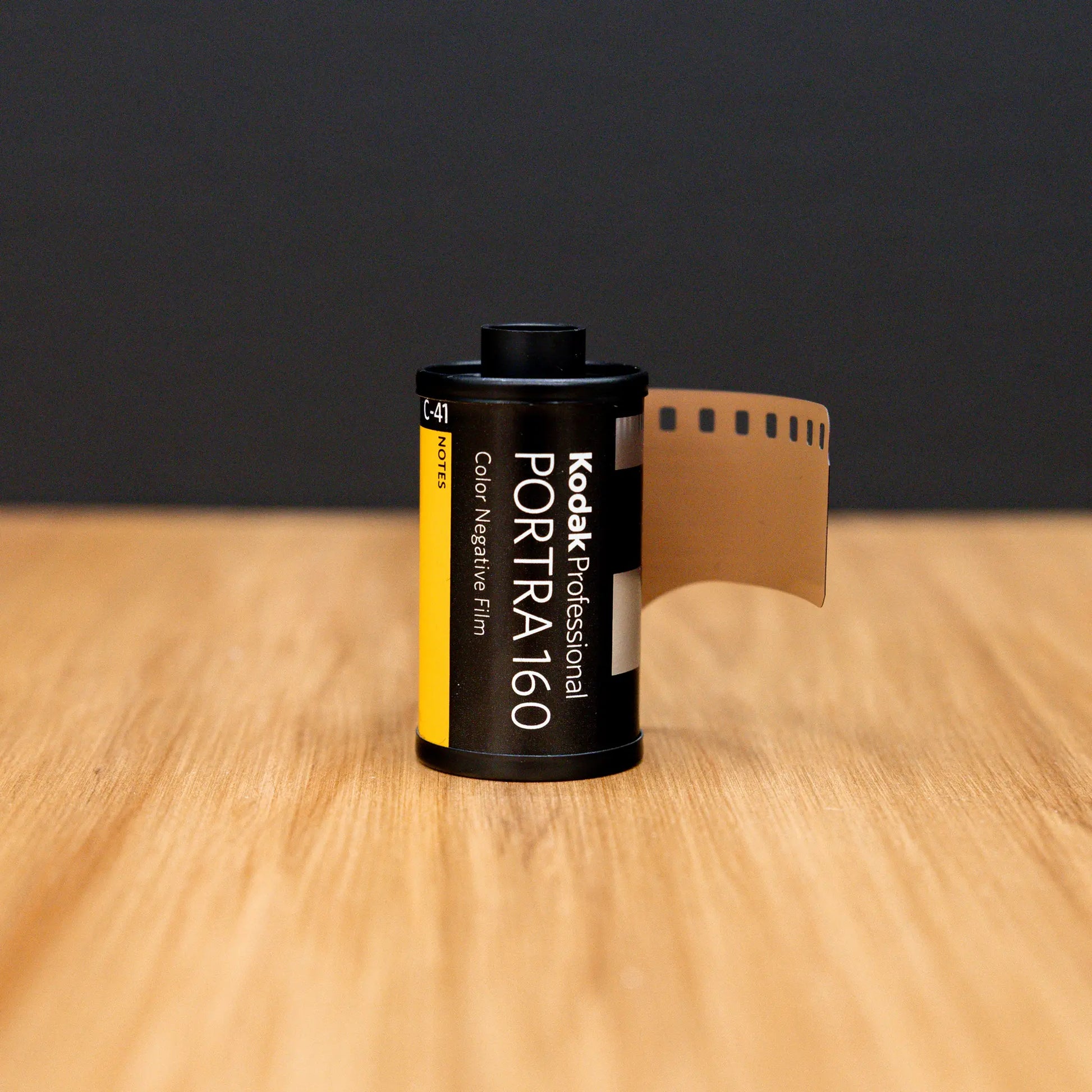 Kodak Portra 160 film canister on a wooden surface with a black background
