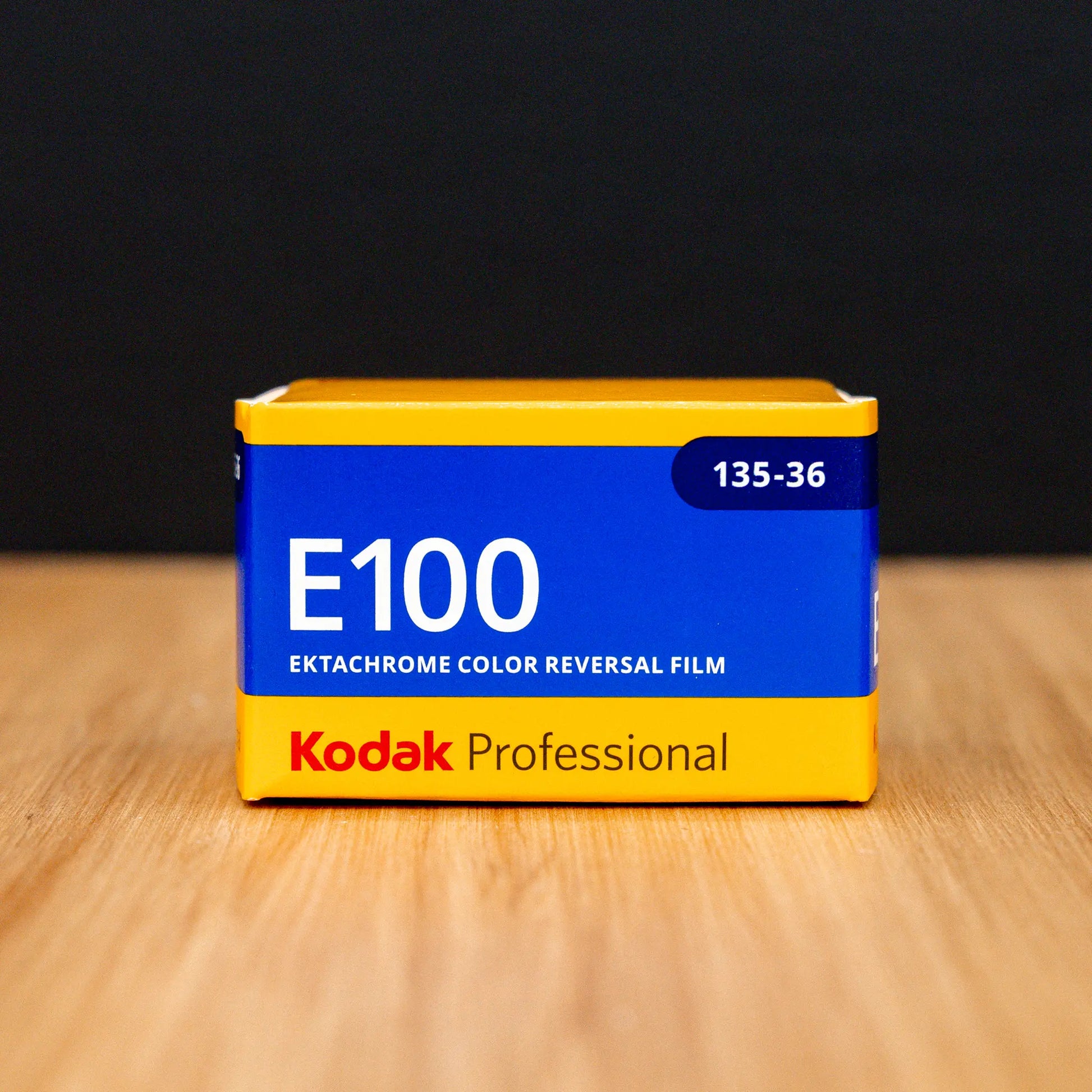 Kodak E100 Ektachrome color reversal film canister on a wooden surface with a black background