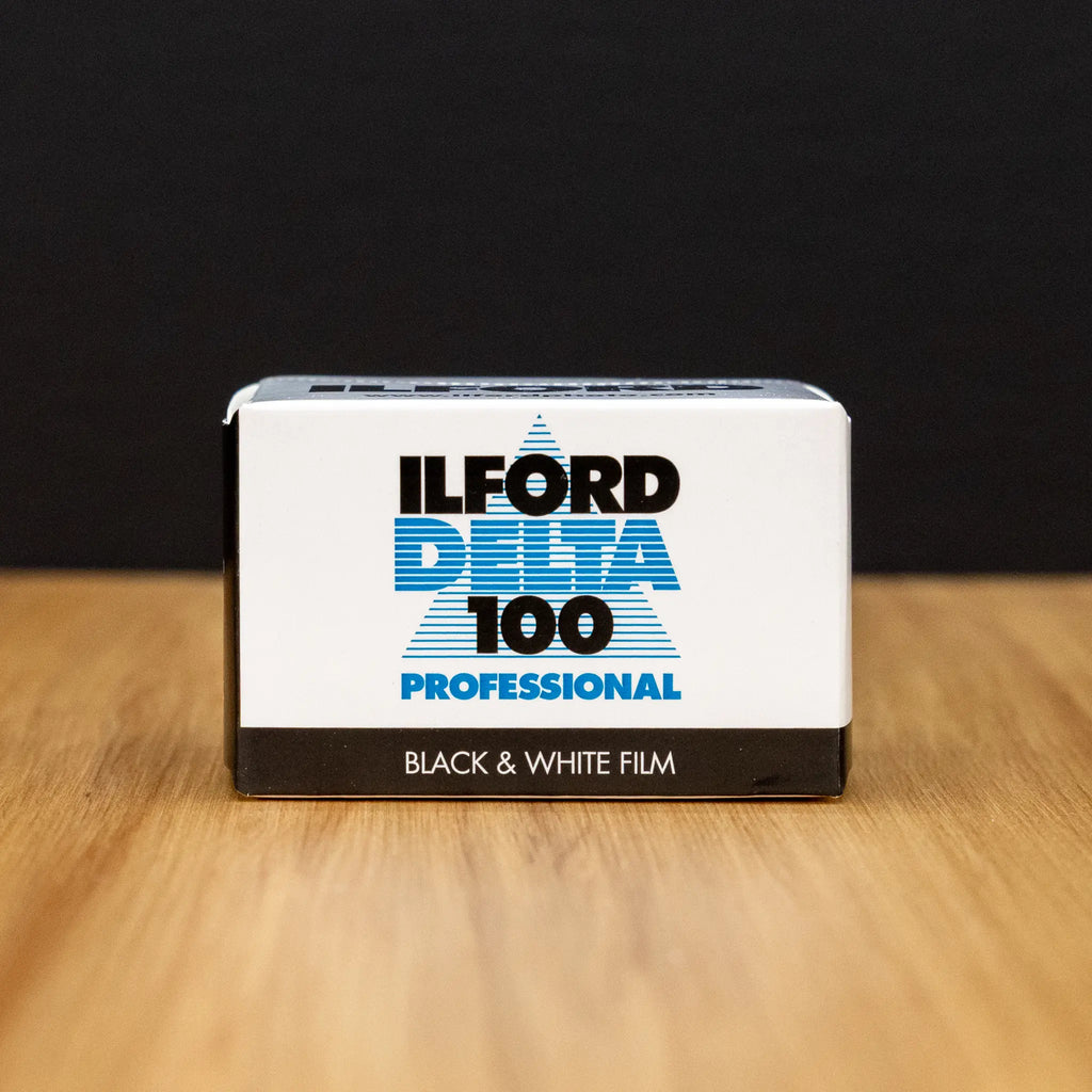Ilford Delta 100 Professional black and white film packaging on a wooden surface with a dark background