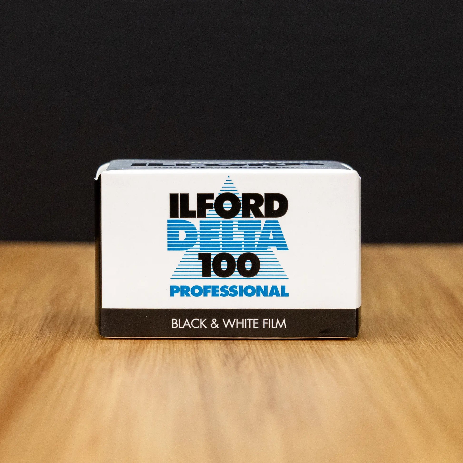 Ilford Delta 100 Professional black and white film packaging on a wooden surface with a dark background