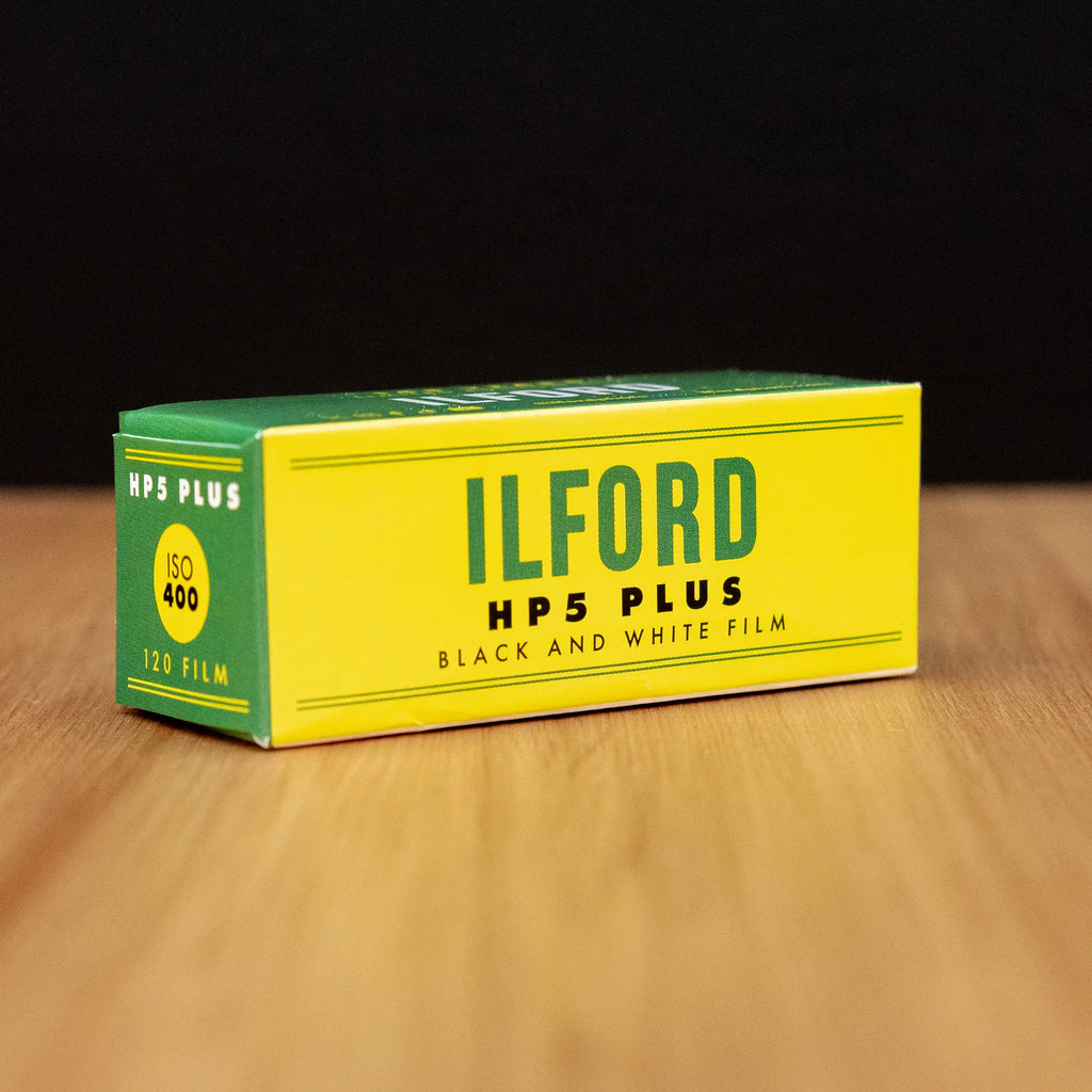 Ilford HP5 Plus black and white film box on a wooden surface with a dark background