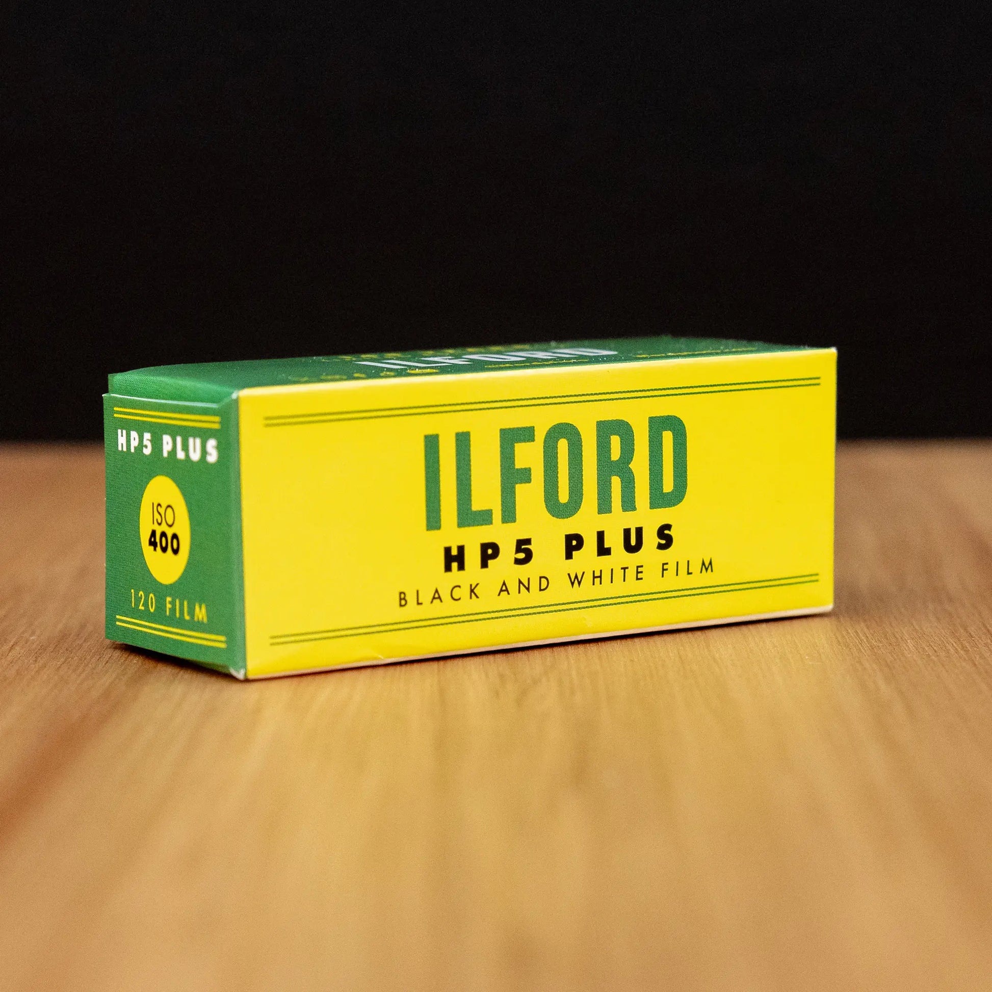 Ilford HP5 Plus black and white film box on a wooden surface with a dark background