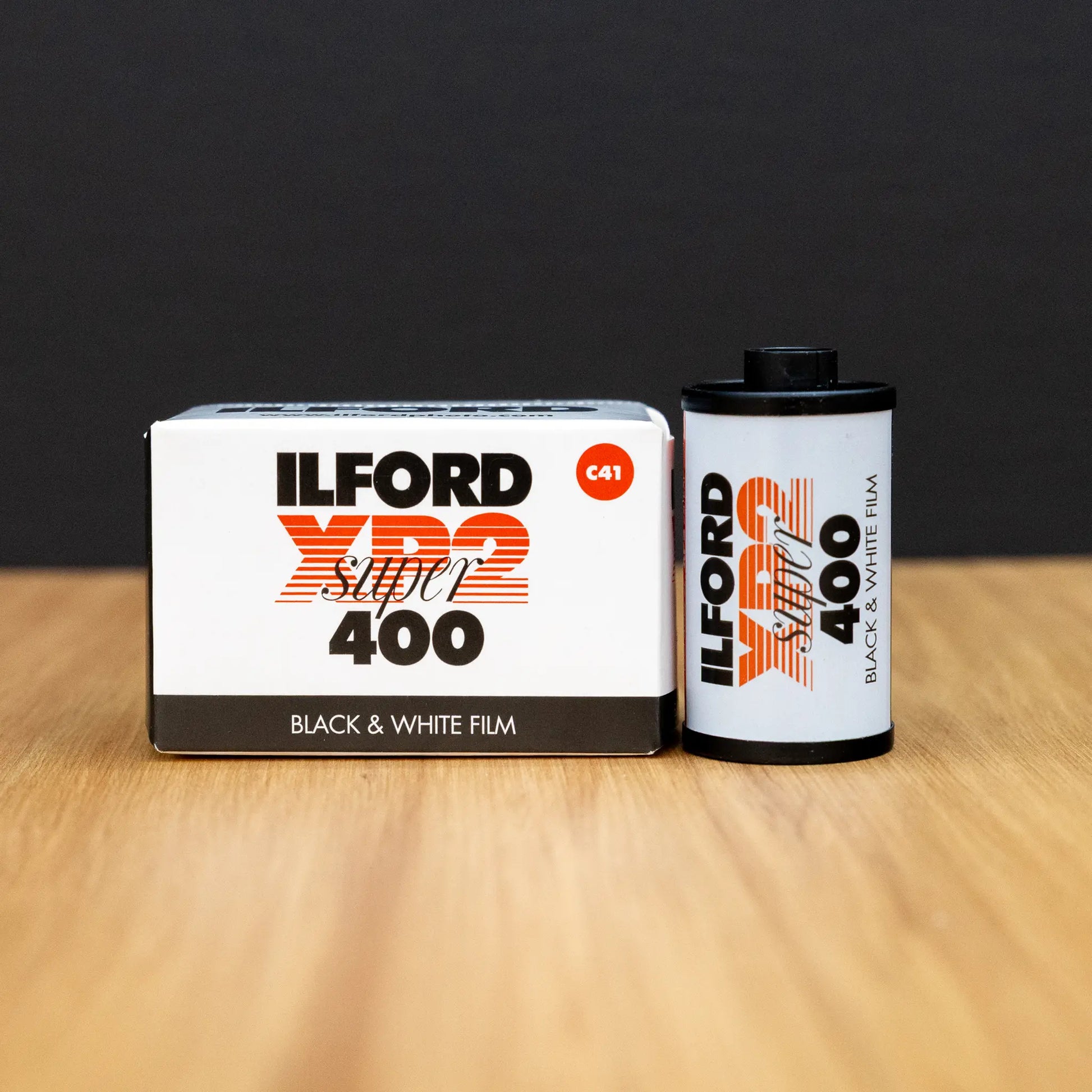 Ilford XP2 Super 400 black and white film canister and packaging on a wooden surface with a dark background