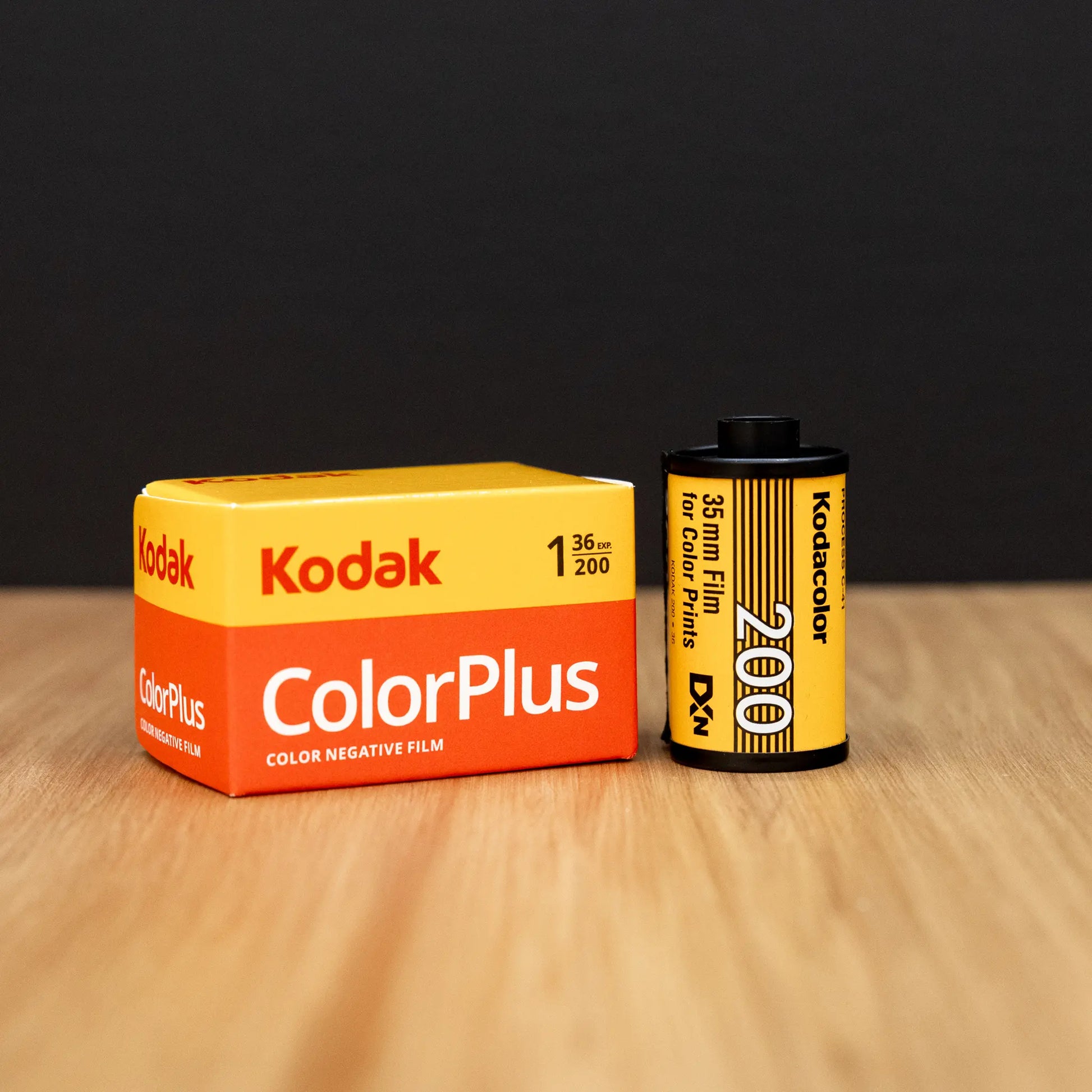 Kodak ColorPlus film canister and packaging on a wooden surface with a black background