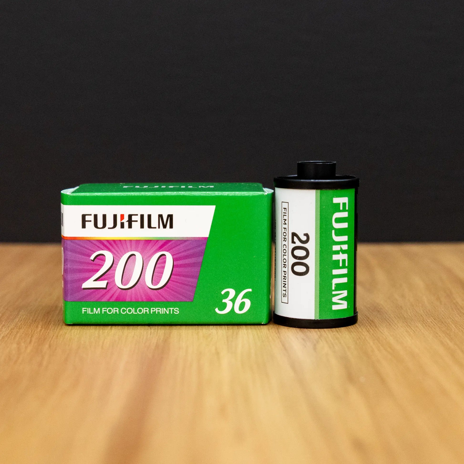 Fujifilm 200 film canister and packaging on a wooden surface with a black background