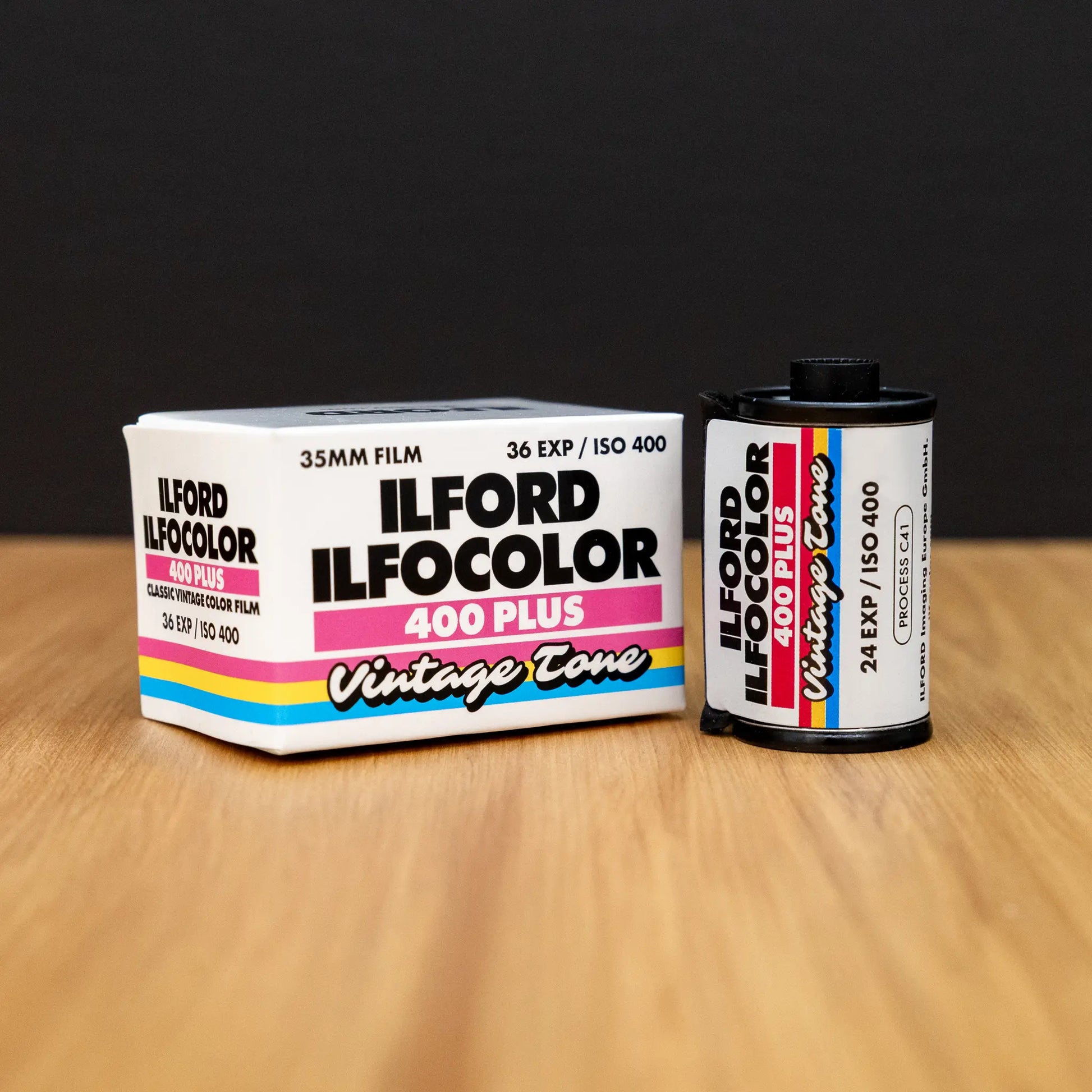 Ilford Ilfocolor 400 Plus film canister and packaging on a wooden surface with a black background