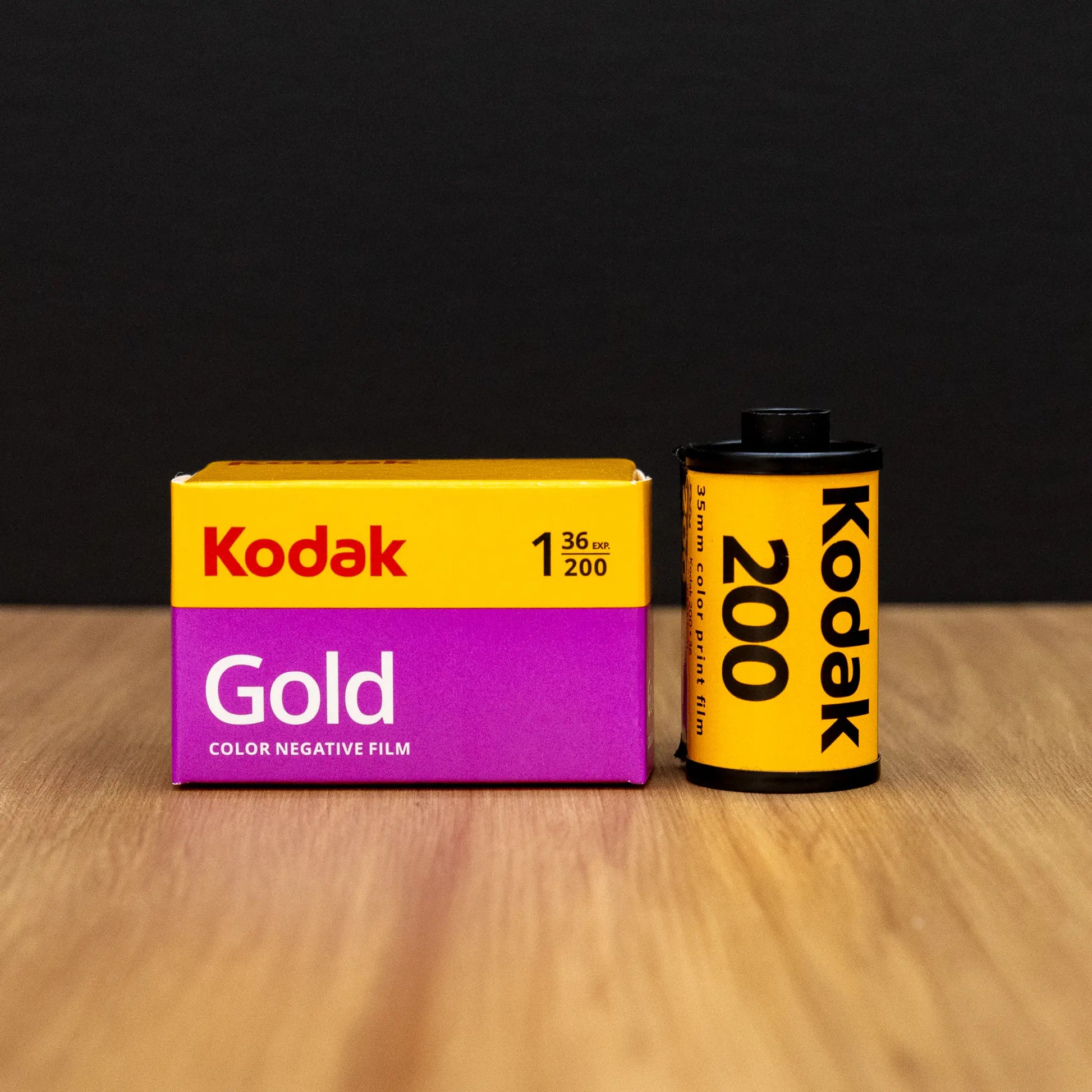 Kodak Gold 200 color negative film box and roll on a wooden surface with a black background