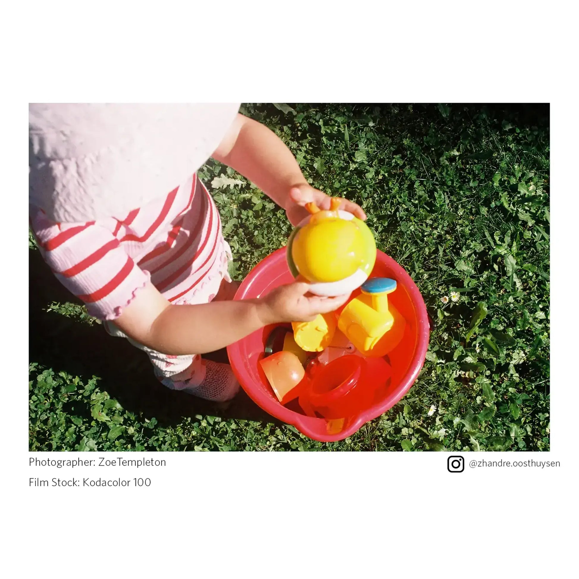 Child playing with colorful toys in a red bucket on grass