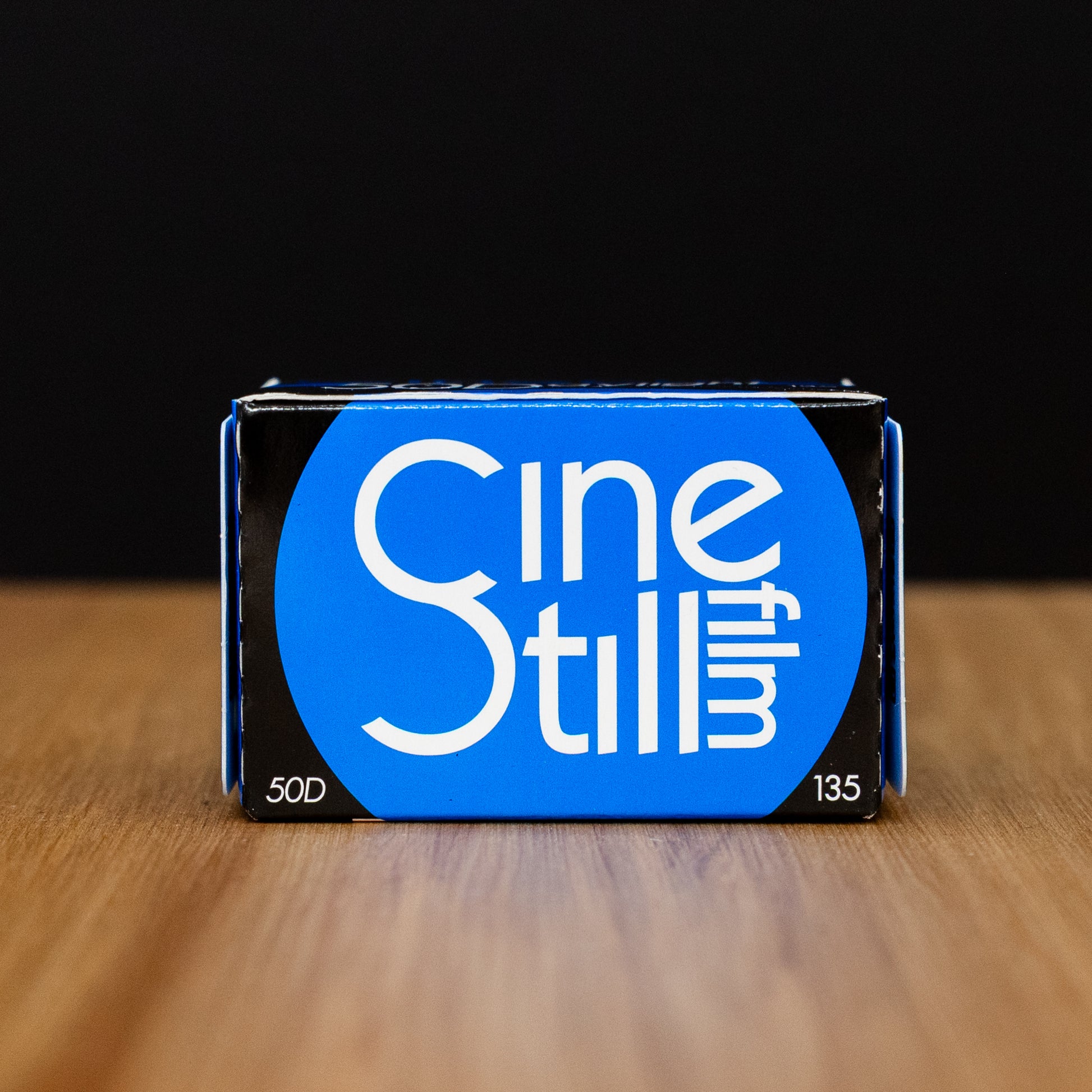 Cinestill 50d product packaging on a wooden surface with a black background