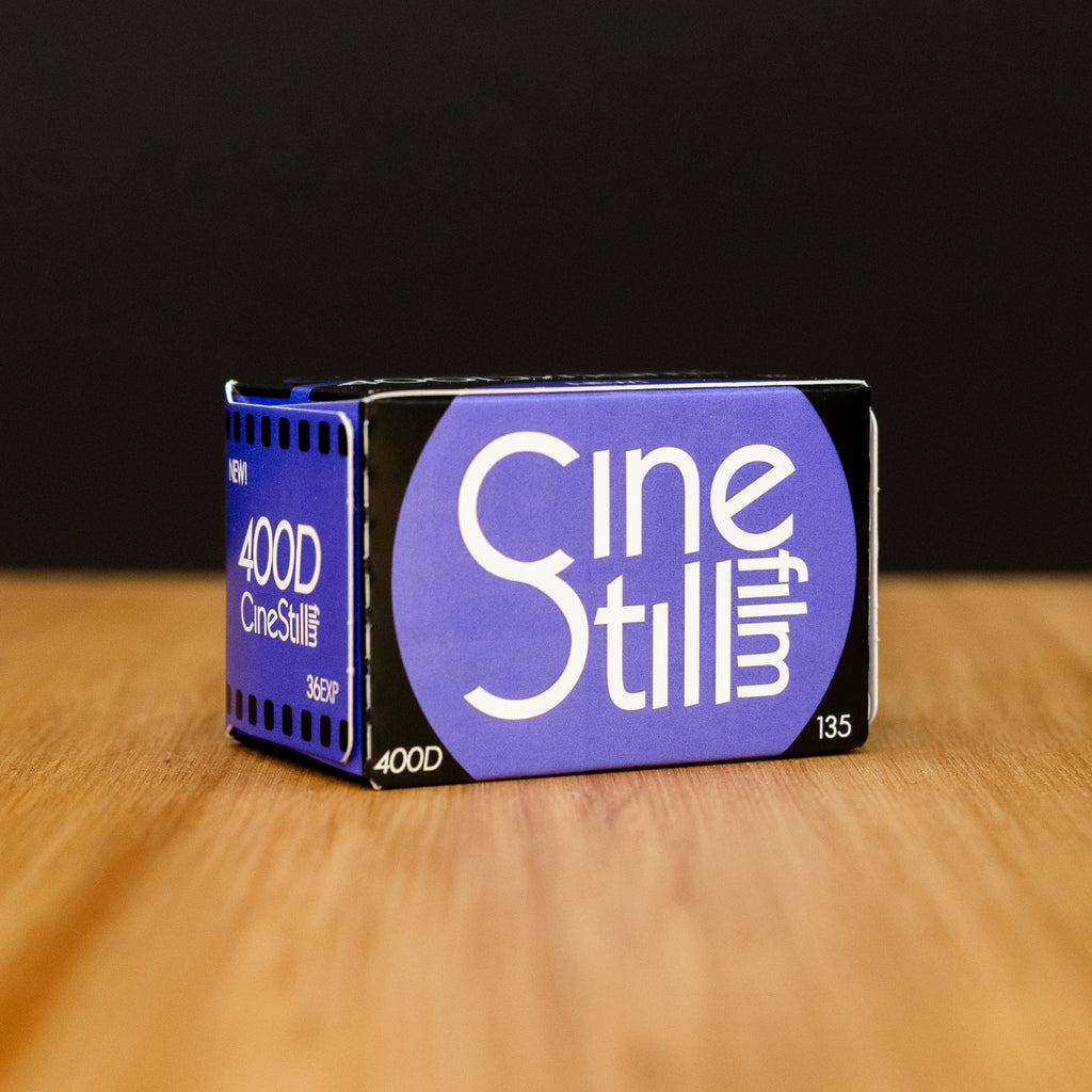 CineStill 400D film canister on a wooden surface with a black background