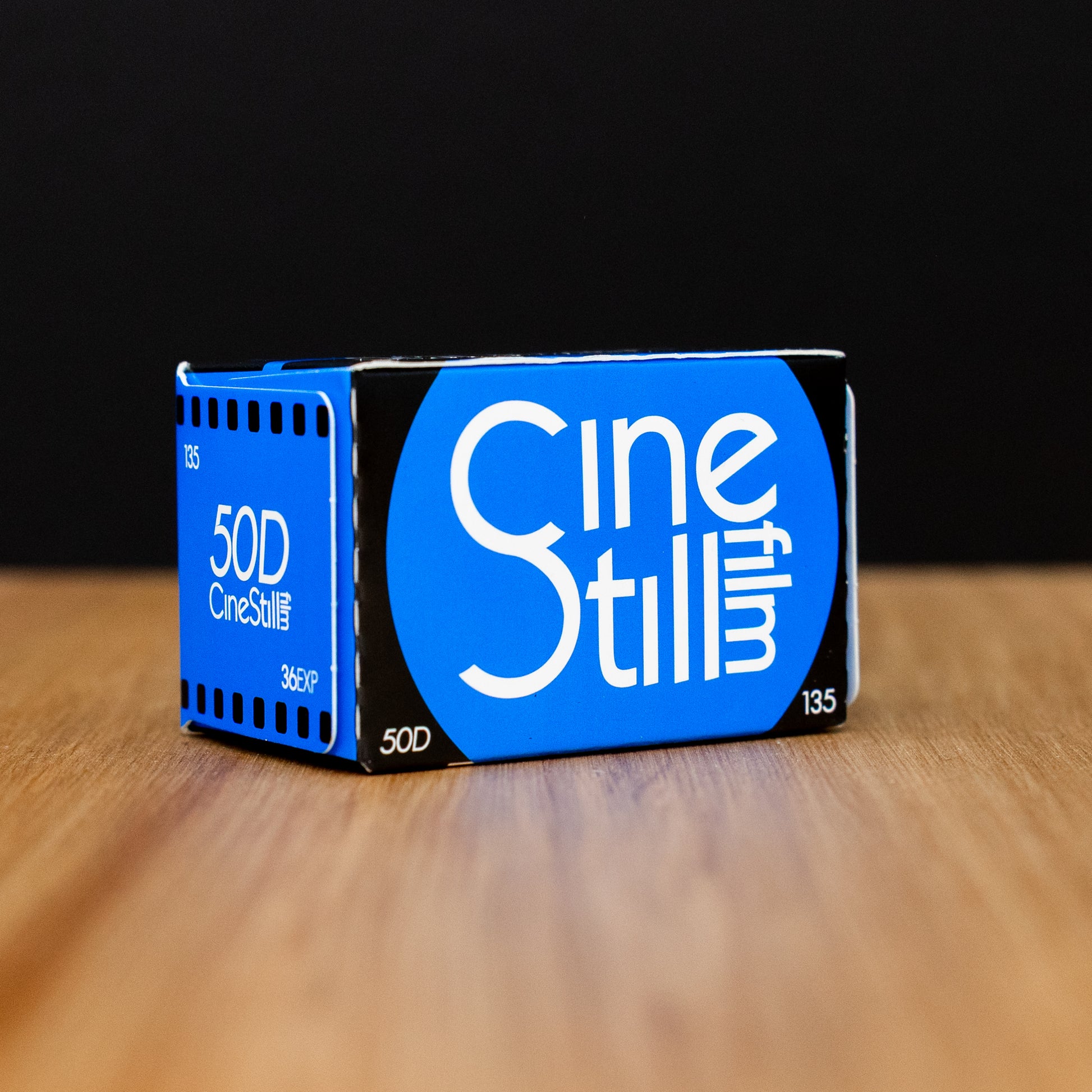 Cinestill 50D film canister on a wooden surface with a black background