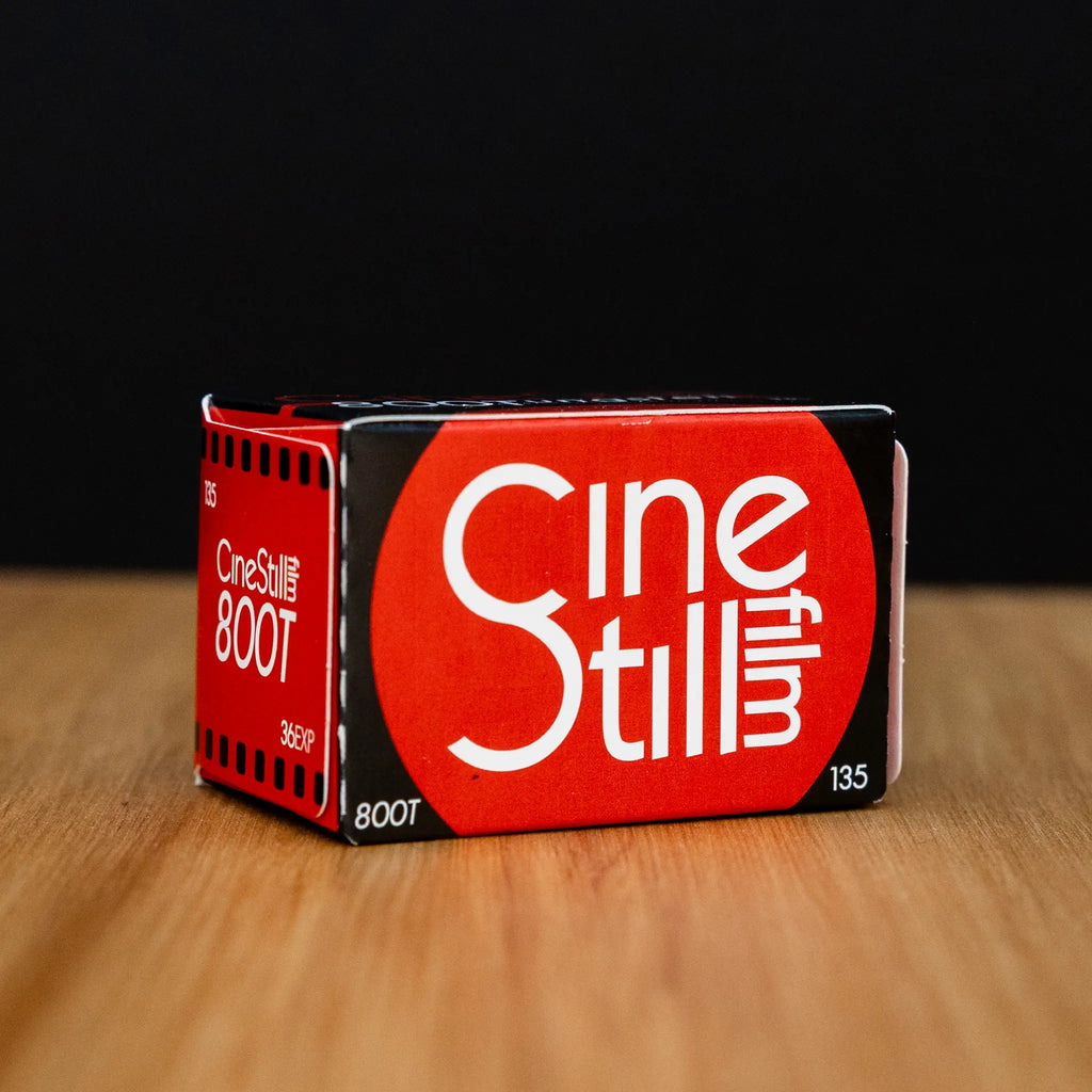CineStill 800T film canister on a wooden surface with a black background