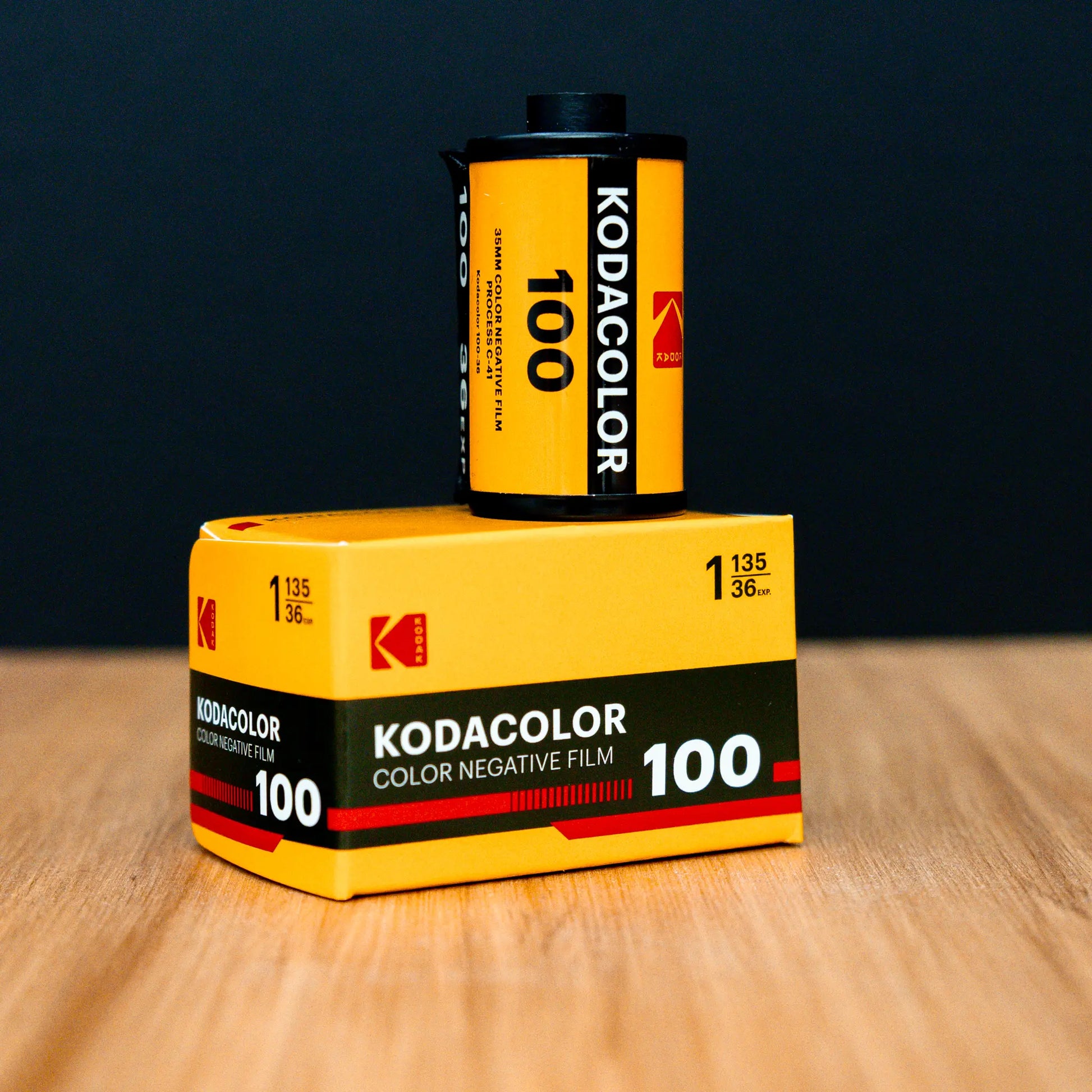 Kodak KODACOLOR 100 film canister and packaging on a wooden surface with a dark background